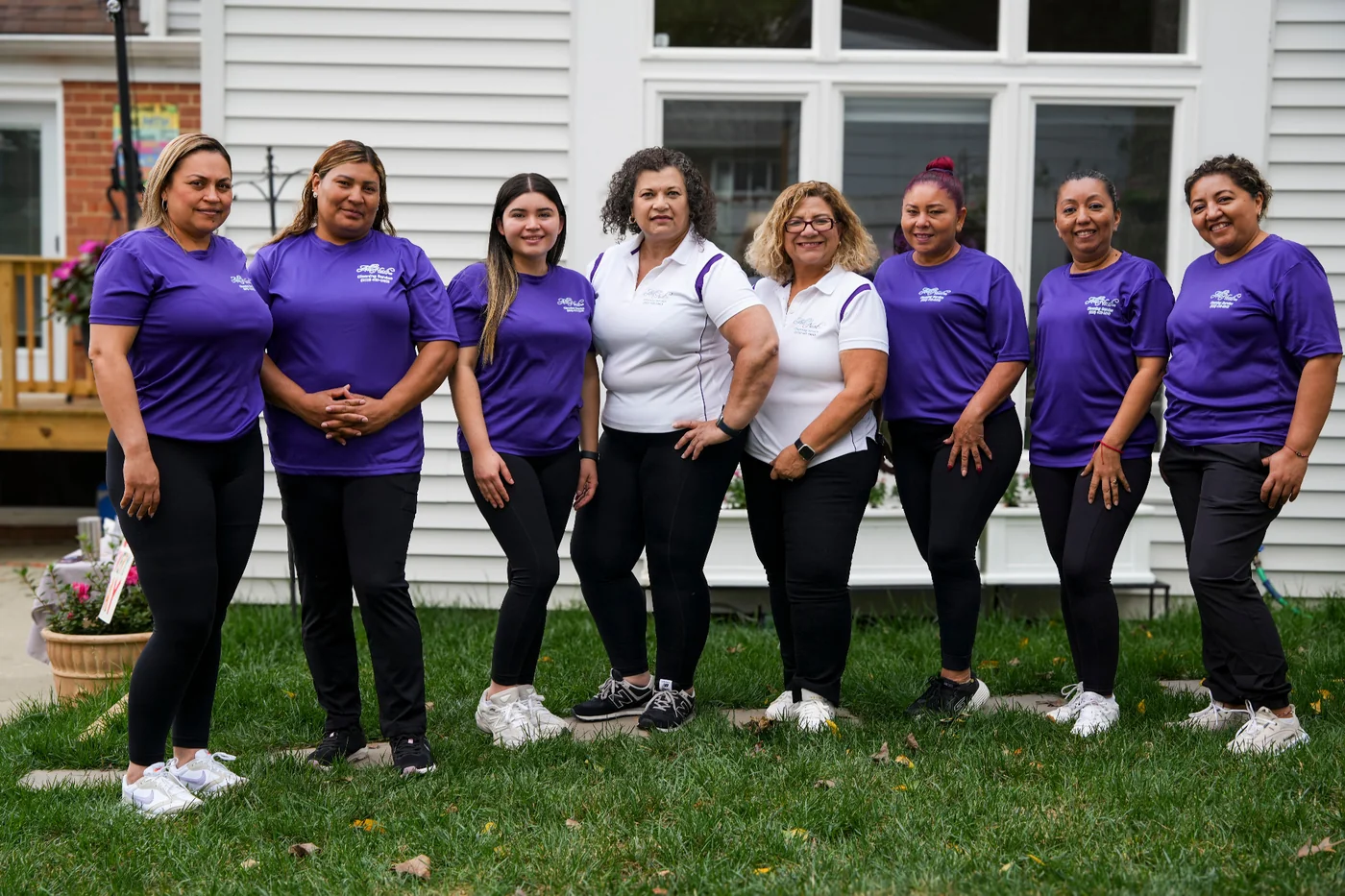 All Neat cleaning team in purple and white uniforms outside a home