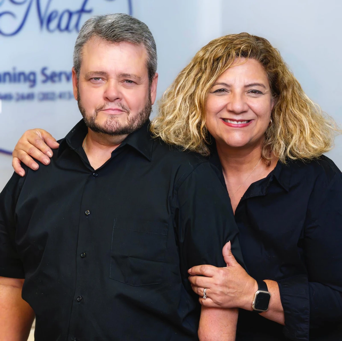 Elisa and Steve pictured together in black shirts in front of the All Neat logo.